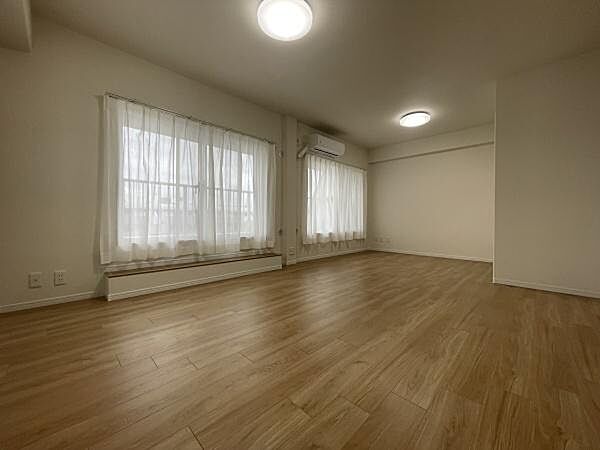 大きな窓からたっぷりと自然光が入る寝室です。落ち着いた色合いのフローリングが印象的です。照明とエアコンも設置されています。窓にはカーテンも付属しています。すっきりとした空間が広がっています。