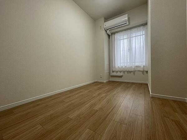 シンプルな内装が特徴で落ち着いた雰囲気が感じられる寝室です。明るい窓から自然光が差し込み清潔感のある空間です。エアコン付きで季節を問わず快適に過ごせます。木目調の床がアクセントになっています。