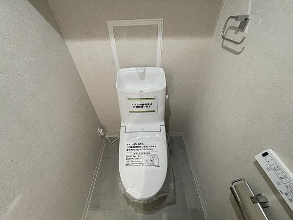 清潔感のあるシンプルなトイレです。壁や床の色合いが落ち着いた雰囲気を演出します。ペーパーホルダーやリモコンも設置されています。ゆとりのある空間設計が特徴です。設備の使いやすさにも配慮されています。