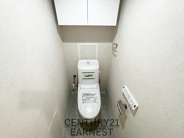 白を基調とした清潔感のあるトイレです。収納スペースが上部にしっかりと確保されています。壁付きのリモコン操作が設置されており使い勝手に配慮されています。すっきりとした内装で落ち着いた空間となっています。