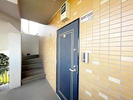 落ち着いた色合いの玄関ドアが印象的です。玄関周りが明るく開放感のある設計です。タイル張りの外壁が清潔感を演出しています。階段や手すりもきれいに整えられています。インターホンが設置されています。