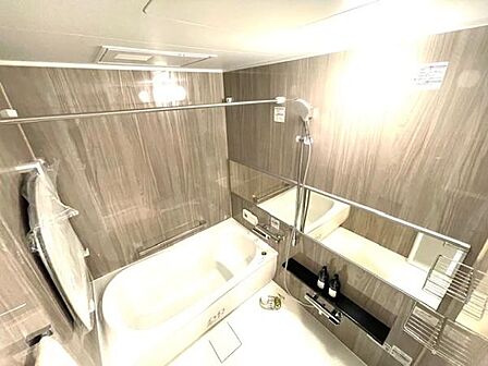 壁面の落ち着いた色合いが特徴的なバスルームです。大きな鏡が空間を広く感じさせます。浴槽とシャワーが分かれていて使い勝手が良いです。収納スペースも設けられており日用品の整理がしやすい設計です。