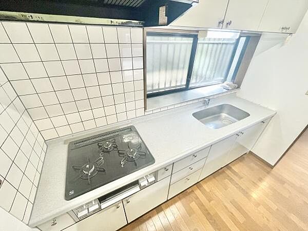 キッチンには広めのワークトップが備わっており作業がしやすい設計です。三口コンロが配置されており調理が効率的です。大きな窓があり明るい雰囲気を感じられます。シンクもゆとりのあるサイズです。