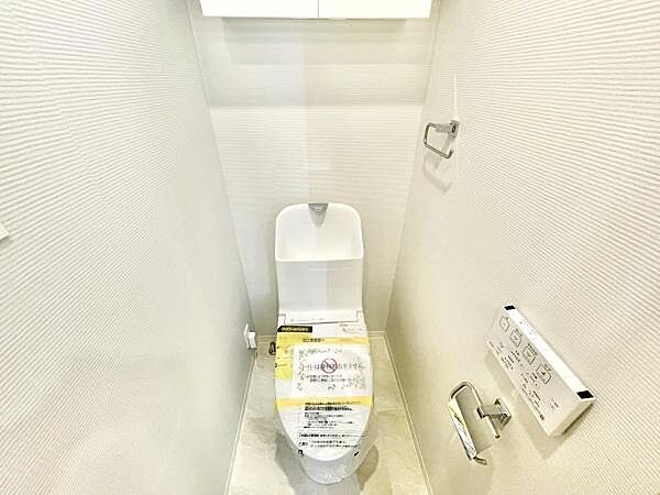 清潔感のあるトイレ空間です。白を基調とした壁と床がすっきりとした印象を与えます。収納棚も設置されており機能性が備わっています。操作パネルやペーパーホルダーも使いやすく配置されています。