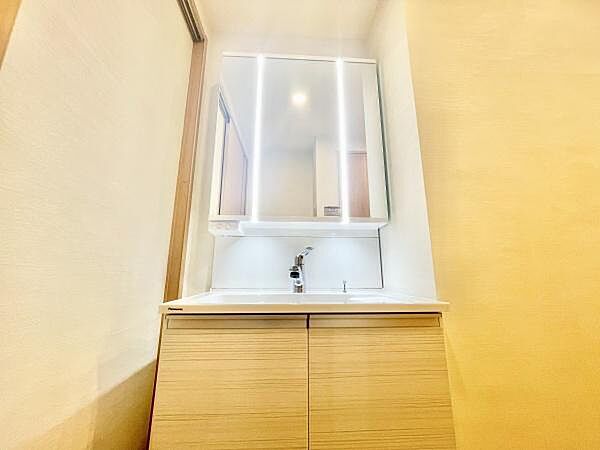 明るい照明付きの洗面台が設置されています。鏡周りもすっきりとしており清潔感があります。収納スペースが下部にあり使いやすいデザインです。シンプルな色合いで幅広いインテリアに馴染みます。