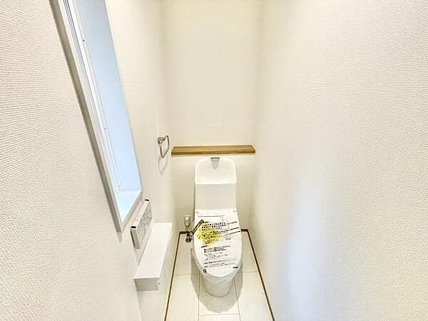 明るい空間に設置されたトイレです。窓があり換気に役立ちます。壁や床は清潔感のあるデザインです。シンプルな設備でお手入れも簡単です。使いやすいペーパーホルダーも設置されています。