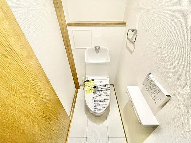 シンプルで清潔感のあるトイレ空間です。収納棚が備え付けられており小物の整理もしやすくなっています。壁付けのペーパーホルダーや操作パネルが使いやすい位置に配置されています。