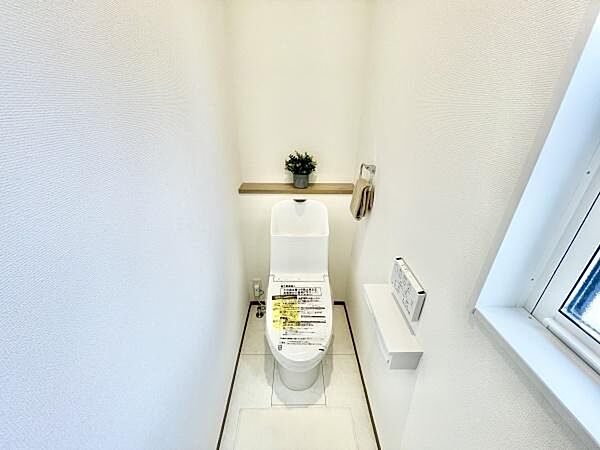窓付きのトイレで明るさを確保しています。清潔感のある白基調の空間です。収納棚がありちょっとした小物も置けます。シンプルなデザインで機能的な印象です。壁面が広く圧迫感を感じにくい設計です。