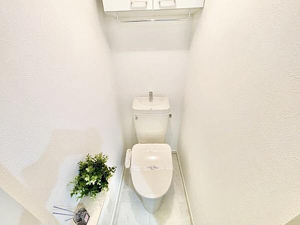 明るい色調でまとめられたトイレ空間です。収納棚が設置されており整理整頓がしやすい設計です。清潔感のある内装で落ち着いた雰囲気が感じられます。観葉植物がアクセントになっています。