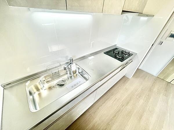 シンプルで洗練されたデザインのキッチンです。広々とした作業スペースが魅力的です。ガスコンロとシンクがバランス良く配置されています。掃除がしやすい素材で清潔感があります。