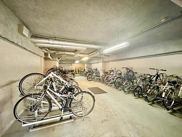 屋内型の自転車置き場が用意されていますので雨や風から自転車を守ることができます。照明が設置されており明るい空間です。複数台の自転車が余裕を持って停められ整理されたレイアウトです。
