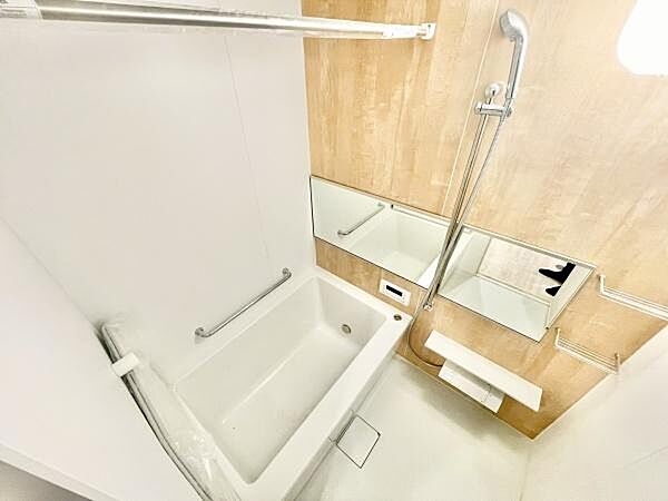 明るい色合いの壁面が特徴的なバスルームです。広めの鏡が空間を広く感じさせます。手すりや収納スペースも設置されており機能的な設計です。浴槽もゆったりとしています。