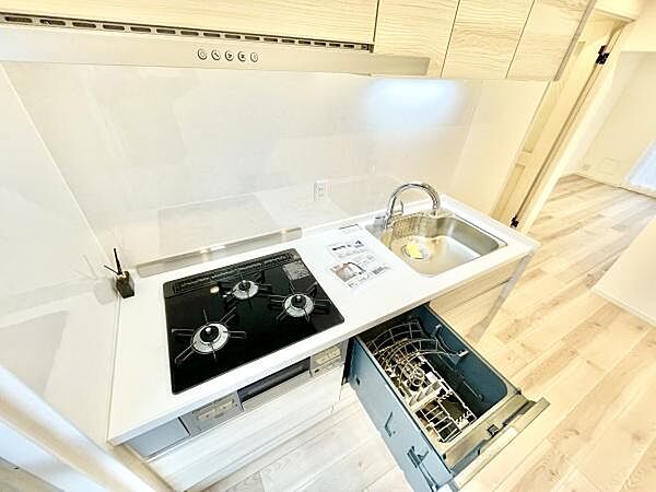 キッチンのカウンターが広々としており複数の調理スペースが確保されています。収納も豊富で整理しやすい設計です。食洗機や三口コンロなど機能性の高い設備が整っています。シンプルなデザインで清潔感があります。