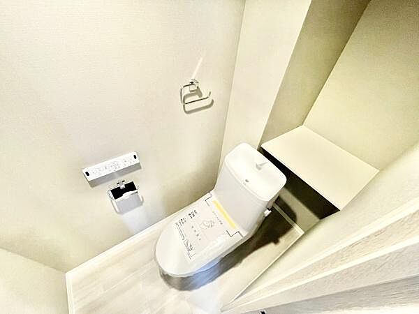 ホワイトを基調とした明るいトイレ空間です。収納スペースが備わっており使いやすさに配慮されています。ペーパーホルダーやリモコン式の操作パネルも設置されています。清潔感あふれる印象です。