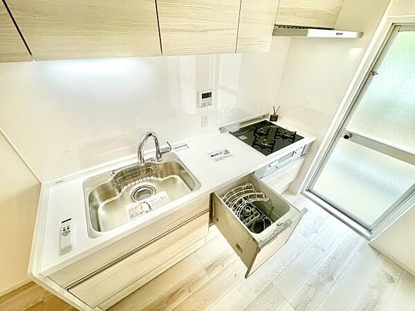 シンプルなデザインのキッチンは白を基調とし清潔感があります。食洗機や三口コンロなど設備も整っています。収納スペースも充実しており使い勝手の良さが感じられます。窓からの自然光が入りやすく明るい空間です。