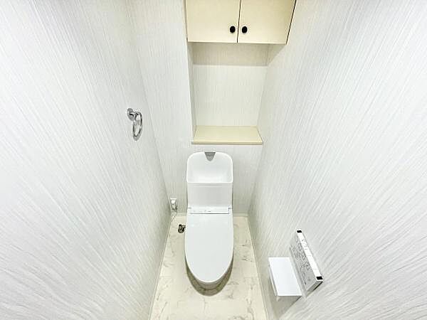 白を基調とした内装で空間全体が明るく感じられます。上部には収納スペースも備わっており整理整頓しやすい構造です。ペーパーホルダーやタオル掛けも設置されており使いやすさが特徴です。