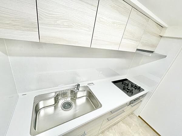 明るい色合いのキッチンで空間が広く感じられます。収納が豊富な上部の棚が使い勝手を高めています。清潔感のあるワークトップが特徴です。ガスコンロも設置されています。