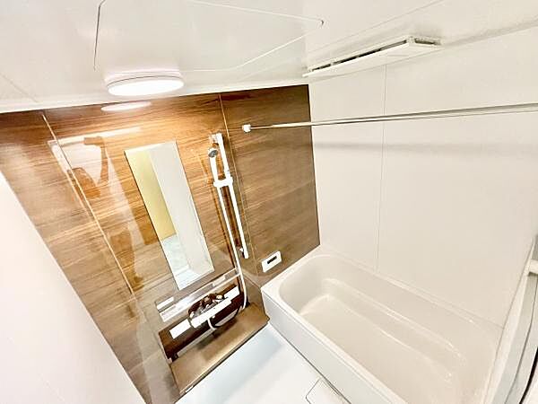 木目調のアクセントパネルが空間に落ち着きを与えます。大きなミラーが浴室を広く感じさせます。浴槽と洗い場のレイアウトが使いやすいです。浴室乾燥用のバーも設置されています。