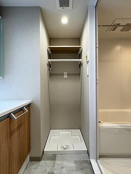 洗面台の隣にある洗濯機置き場です。上部に棚とハンガーパイプが備わり、洗剤や小物を置きながら乾いたタオルを掛けておくこともできます。