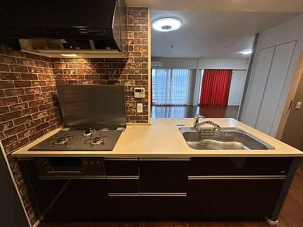 レンガ調のタイルが壁面を引き締める対面式キッチンです。ビルトイン食洗機を備え、洗い物の時間を短くして家族との会話に充てられます。手元の作業も見渡しやすい配置になっています。