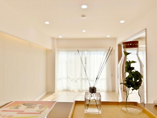 大きな窓から陽光が差し込む明るいリビング。ダウンライトと壁面の間接照明が優しく空間を包み込み、夜は上質な寛ぎ時間を演出します。