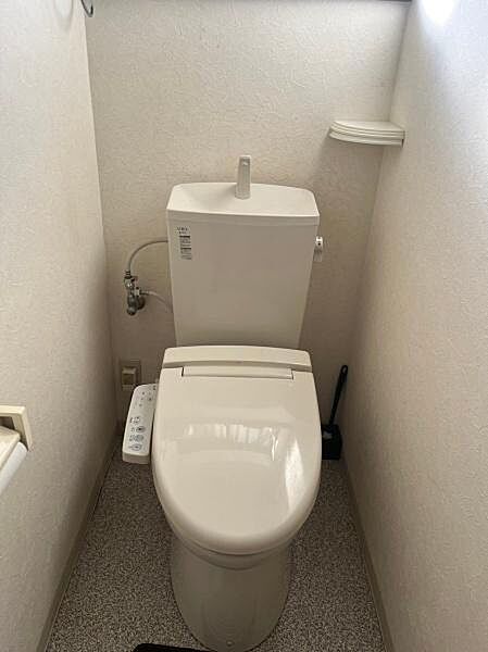 シンプルですっきりとしたデザインのトイレです。壁付きの収納棚が設置されています。温水洗浄機能つきの便座が備わっています。コンパクトな空間にまとめられています。お掃除用具も収納可能なスペースです。