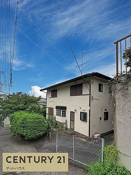 青空の下建物が明るく映えている現地写真です。前面道路がしっかりと確認できるため周囲の状況も把握しやすいです。門扉や植栽も整えられ全体的に落ち着いた印象です。電線や周辺環境もしっかりと写っています。
