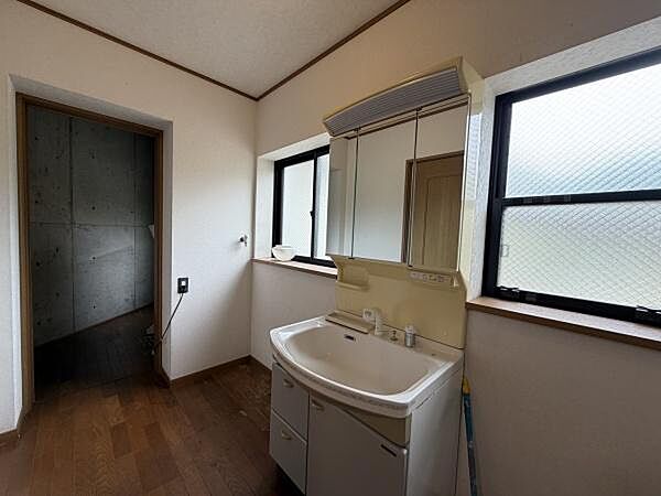 2面の窓から自然光が差し込む洗面所です。収納力のある洗面台は日常の使い勝手を意識した造りです。広々としたスペースが確保されています。木目調の床が空間に落ち着いた印象を与えます。