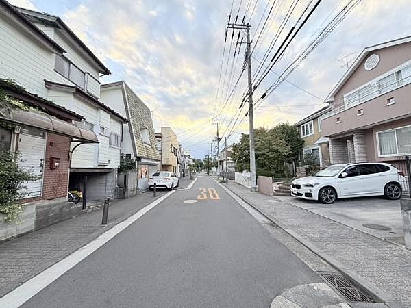 整然と並んだ住宅街の雰囲気が広がっています。落ち着いた街並みが感じられる環境です。歩道も確保されており安心感があります。季節感のある空が印象的です。