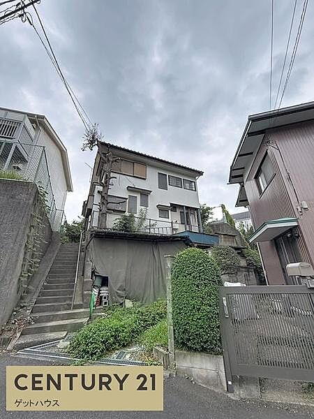 落ち着いた住宅街に佇む現地写真です。前面道路までのアプローチが確保されています。周囲には建物が立ち並び住環境が整っています。階段や植栽があり敷地へのアクセスもスムーズです。