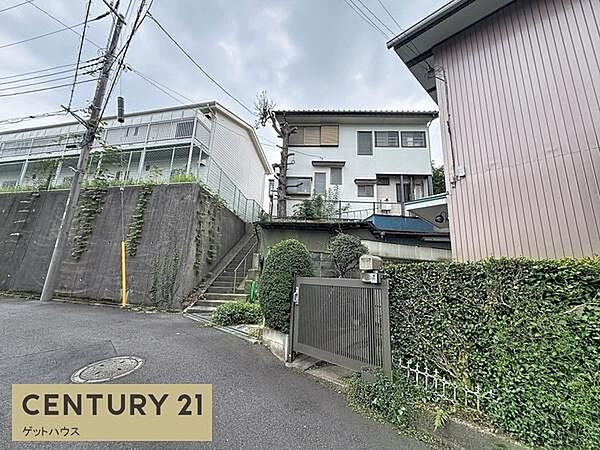 前面道路を含む現地写真です。周囲には塀や緑があり落ち着いた雰囲気となっています。現地の様子がしっかりと確認できます。道路の幅や勾配も写真から把握できます。駐車スペースへのアプローチも視認可能です。