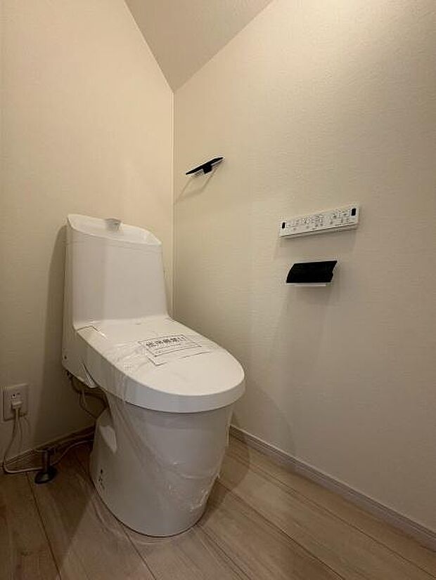 シンプルで清潔感のあるトイレ空間です。壁面にリモコンやペーパーホルダーが設置され使い勝手に配慮されています。フローリングの色合いが落ち着いた雰囲気を演出しています。