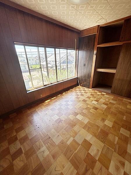 大きな窓から自然光がたっぷりと入る洋室です。木目調の壁と床が温かみのある雰囲気を演出しています。収納スペースも備えており荷物の整理に便利です。開放感のある空間が広がっています。