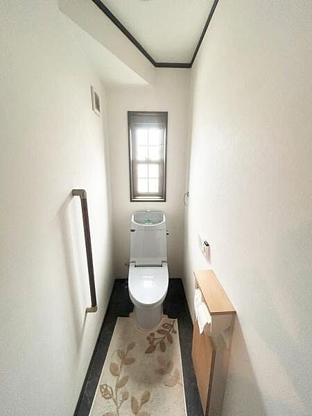 【一部AIモノ消し済み・実際の室内状況優先】窓付きで明るさを感じられるトイレです。手すりが設置されているため安心して利用できます。ペーパーホルダーも設置されています。
