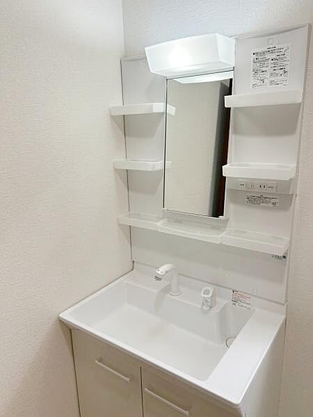 収納力に優れた棚が備わった洗面台です。シンプルなデザインで空間をすっきり見せます。清潔感のある白を基調とした仕様となっています。ミラー上部には便利な照明付きです。日々のお手入れがしやすい設計です。