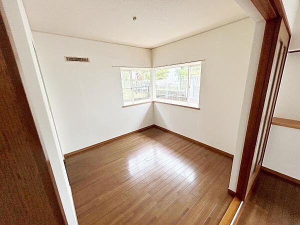 明るい光が差し込む角部屋で窓から外の景色を楽しめます。木目調のフローリングが温かみのある空間を演出します。シンプルな内装で家具のレイアウトも自由に考えられます。開放感のある洋室です。