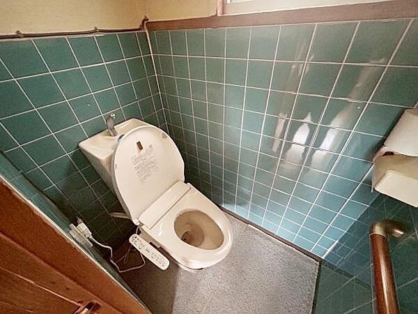 グリーンのタイルが特徴的なトイレです。ウォシュレット付きで快適にご利用いただけます。手すりが設置されており利便性が考えられています。