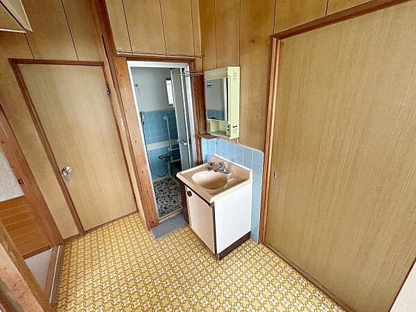 シンプルな洗面台が設置されており使いやすいスペースです。木目調の壁と床で温かみのある雰囲気です。バスルームと隣接しているため移動も便利です。収納付きの鏡が設置されています。