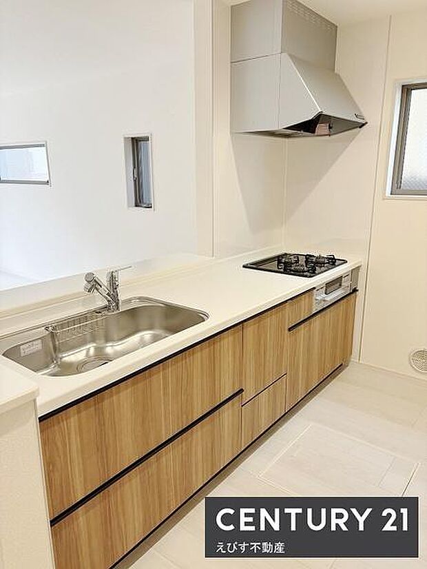 清潔感のある白を基調とした内装に木目の扉が調和したキッチンです。ガスコンロや広めのシンクが備わっていて快適にご利用いただけます。スリムな換気フードもあり空間をすっきりと見せています。