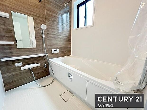 木目調のアクセントパネルが印象的なバスルームです。大きな窓があり明るい空間を演出しています。浴槽が広く清潔感のある内装が特徴です。浴室乾燥機や手すりなど機能的な設備も備えています。