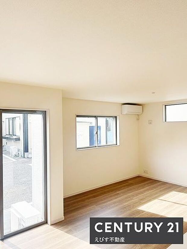 リビングは明るい光が差し込む大きな窓が特徴です。床はナチュラルな色合いで空間が広く感じられます。エアコンも設置されています。壁面や窓の配置がすっきりとしており使いやすい空間です。