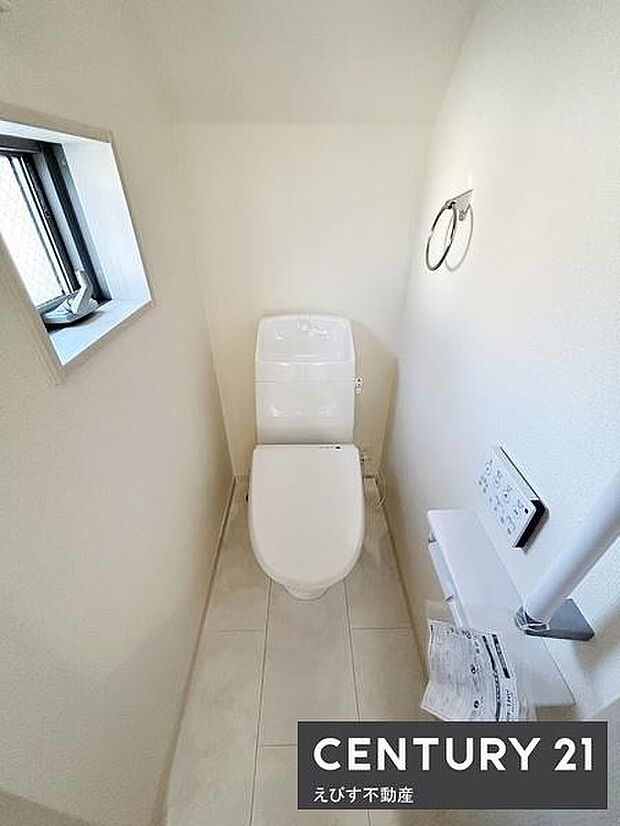 清潔感のあるトイレ空間です。小窓が設けられていて換気に便利です。壁にはペーパーホルダーやリモコンが設置されています。床は明るい色合いで空間を広く見せます。シンプルで使いやすいデザインです。