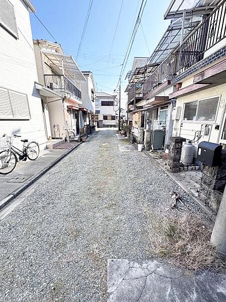 周囲に住宅が並ぶ静かな環境が広がっています。前面道路は車の往来も安心できる幅です。自転車も停めやすいスペースが確保されています。日当たりの良さも感じられる現地写真です。