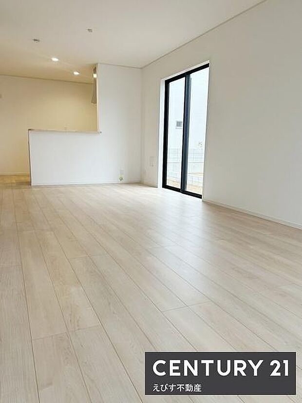 明るいフローリングが印象的なリビングです。大きな窓から光が差し込み開放的な空間を実現しています。白を基調とした内装がすっきりとした印象を与えます。キッチンとのつながりも感じられるレイアウトです。