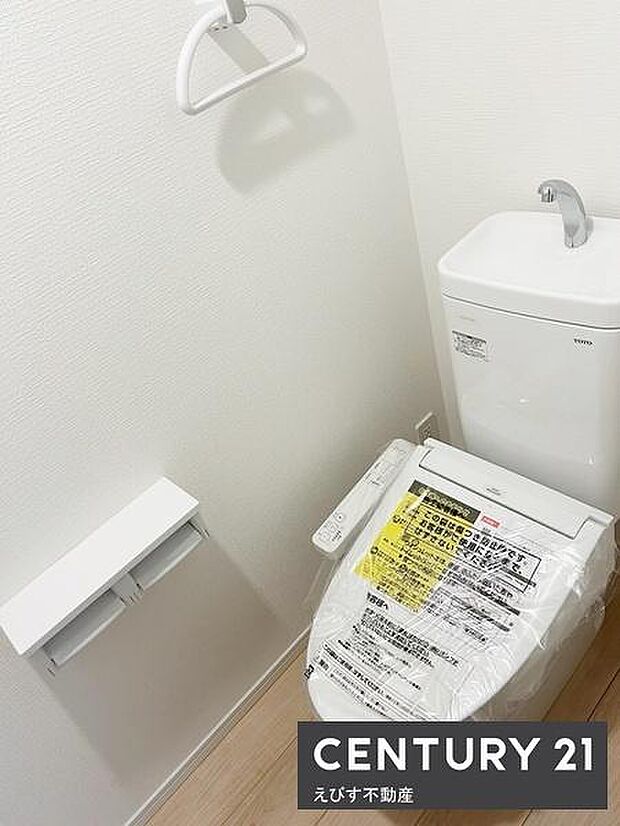 白を基調とした清潔感のあるトイレスペースです。新しい温水洗浄便座が設置されています。備え付けのペーパーホルダーやタオル掛けも使いやすい配置です。手洗い付きで機能性にも配慮されています。