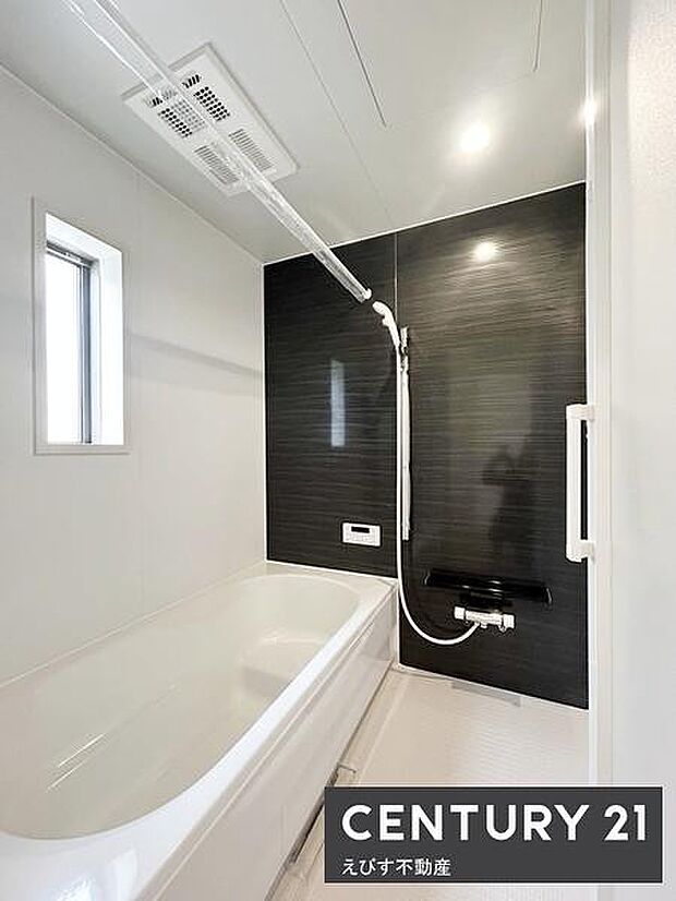 浴室の壁面にはアクセントパネルが使用されモダンな印象を演出しています。窓付きで換気がしやすく清潔感のある空間です。浴槽はゆったりサイズで落ち着いた雰囲気が特徴です。シャワーや収納棚も完備されています。