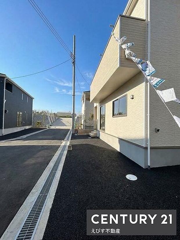 黒色の舗装が敷かれておりメンテナンスがしやすい外構です。隣接する建物や境界フェンスも整っています。シンプルな植栽が端に配されておりすっきりとした印象です。建物との距離感も適度です。