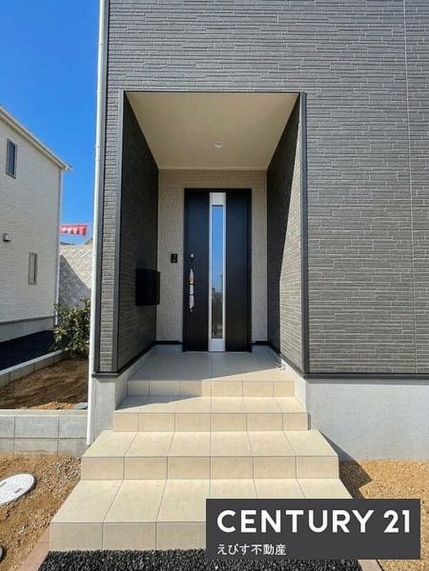 玄関はシンプルなデザインで落ち着いた色合いが外観に調和しています。段差が緩やかでアクセスしやすい造りです。軒下スペースが設けられており天候による影響も受けにくくなっています。