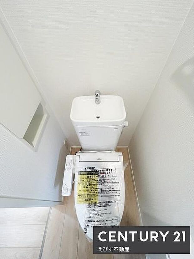 コンパクトな空間に清潔感のあるトイレが設置されています。手洗い器一体型のタンクで使い勝手にも配慮されています。シンプルな内装が明るい印象を与えています。収納スペースも確保されている点がポイントです。