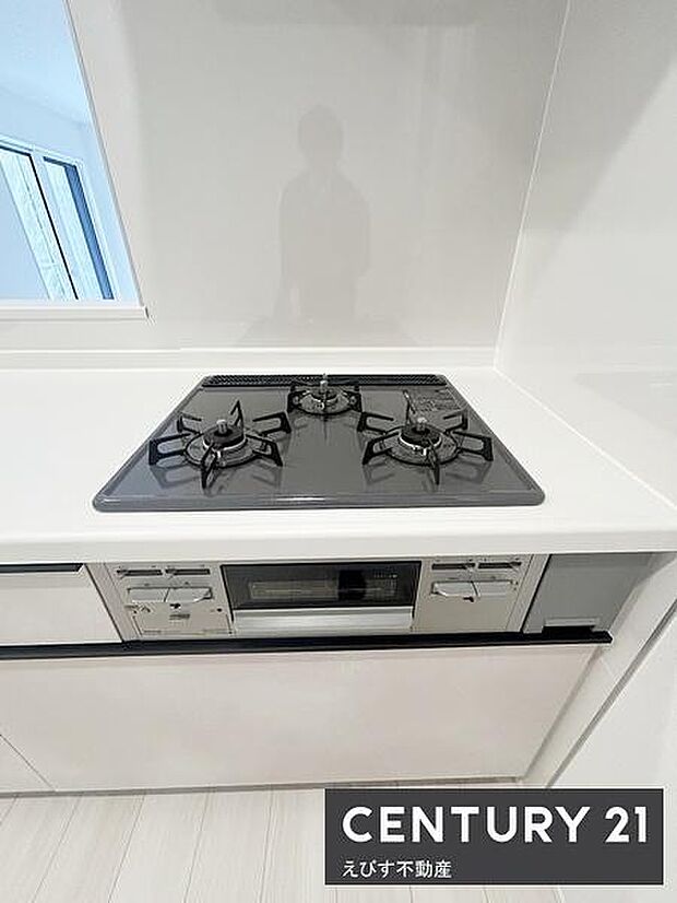 三口コンロを備えたキッチンです。シンプルで清潔感のあるデザインが特徴です。作業スペースも確保されており使いやすい配置となっています。収納も充実しています。毎日の調理に便利です。